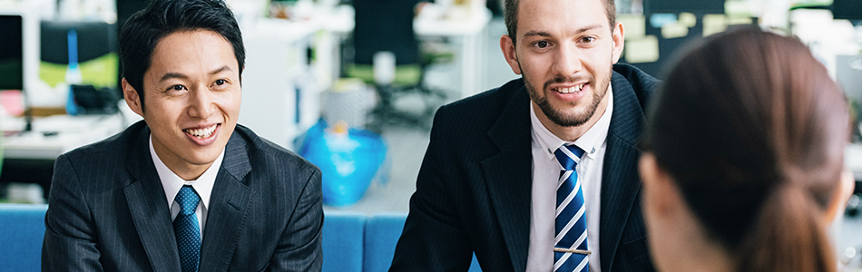 ネイティブのビジネスマンとともに笑顔で交渉を行う日本人男性ビジネスマンの写真